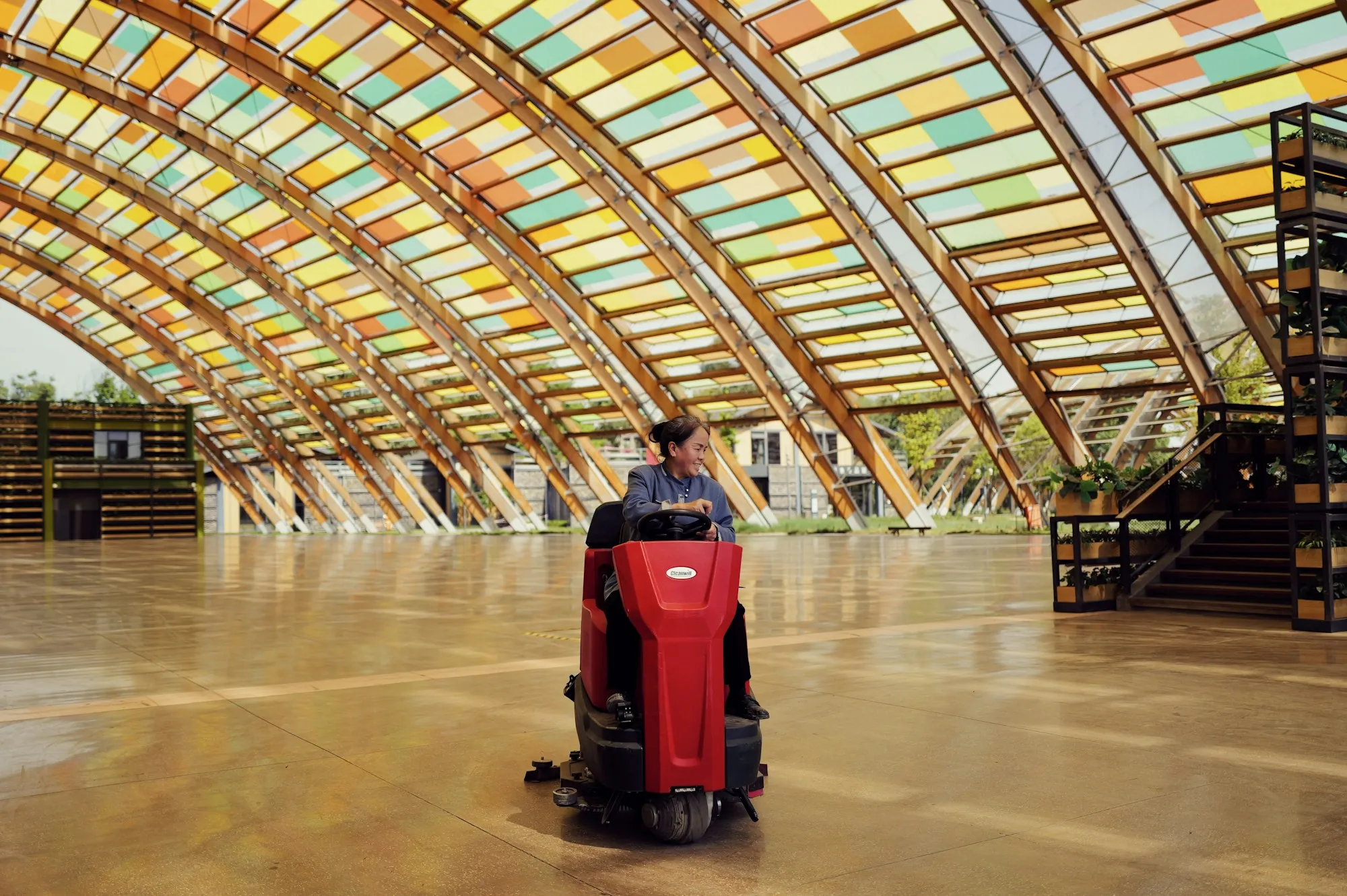 Operator driving a floor scrubber across a large hall
